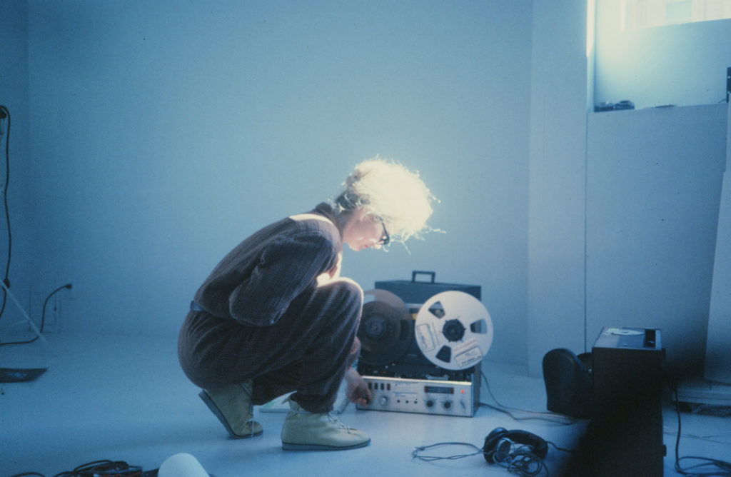 A person is bent over and interacting with a reel to reel tape recorder.